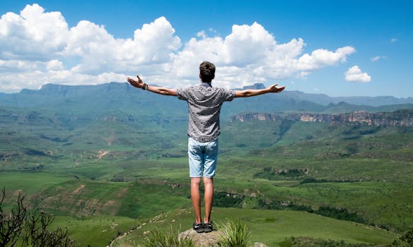 Spirituality and Law of Attraction - A man stands triumphantly with arms open, overlooking a scenic mountain range.