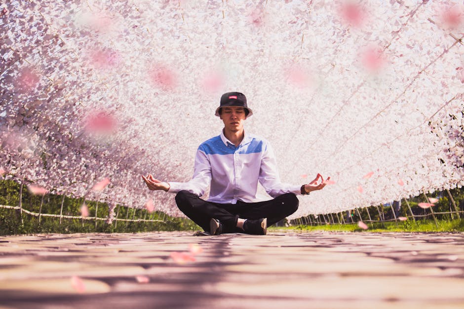 A young man in a hat meditates in a vibrant outdoor floral tunnel, embodying serenity and fashion.