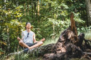 Young man practicing meditation on tree log in calm Berlin forest.