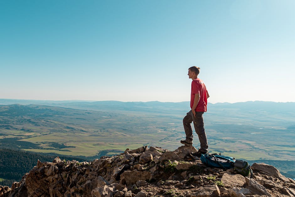 Man standing on mountain peak, admiring landscape on a sunny day, perfect for adventure and travel themes.