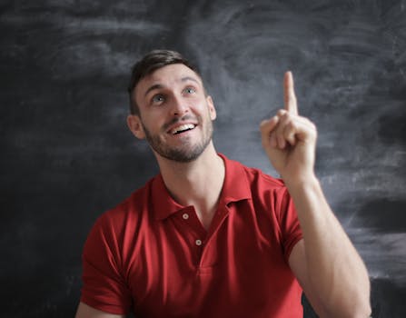 The Silva Ultramind System Review - Happy young man in a red polo shirt smiling and pointing upwards in front of a blackboard.