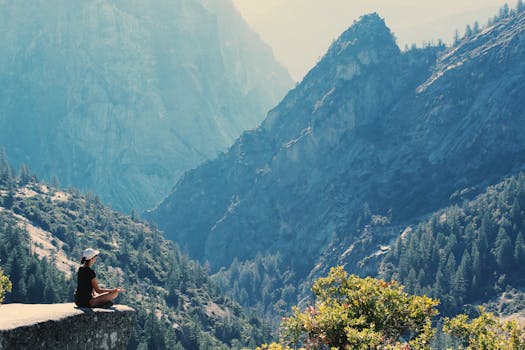 Spirituality and Law of Attraction - A woman practices meditation on a cliff edge, surrounded by majestic mountains and serene nature.