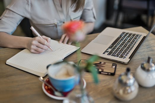 Manifestation Journaling: How to Apply and Key Methods Manifestation Journaling - Woman writing in a notebook with a laptop and coffee cup on a desk. Ideal for workspace inspiration.