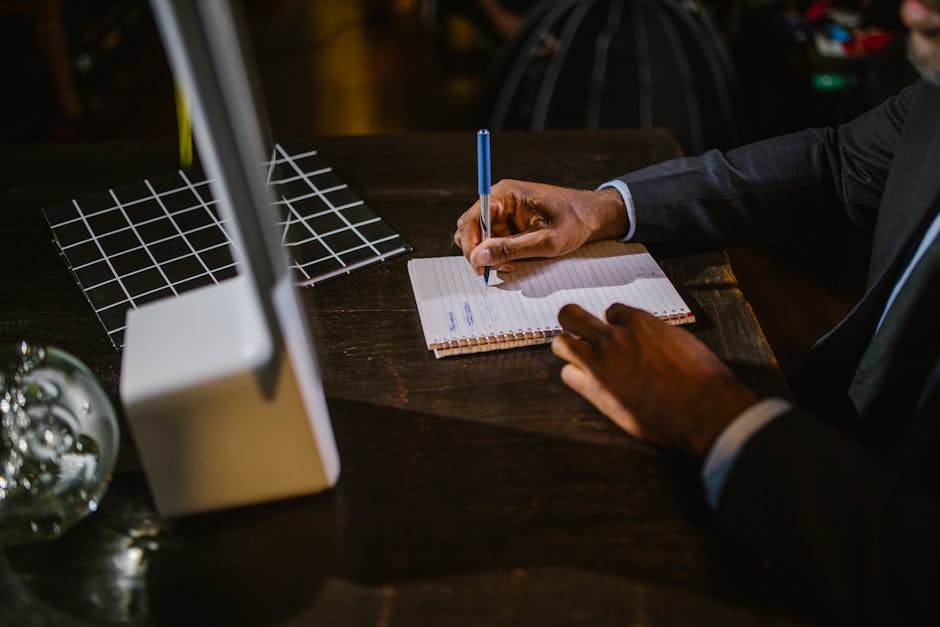 Best manifestation courses - A businessman in a suit writing notes on a notebook at a desk, suggesting a professional office environment.