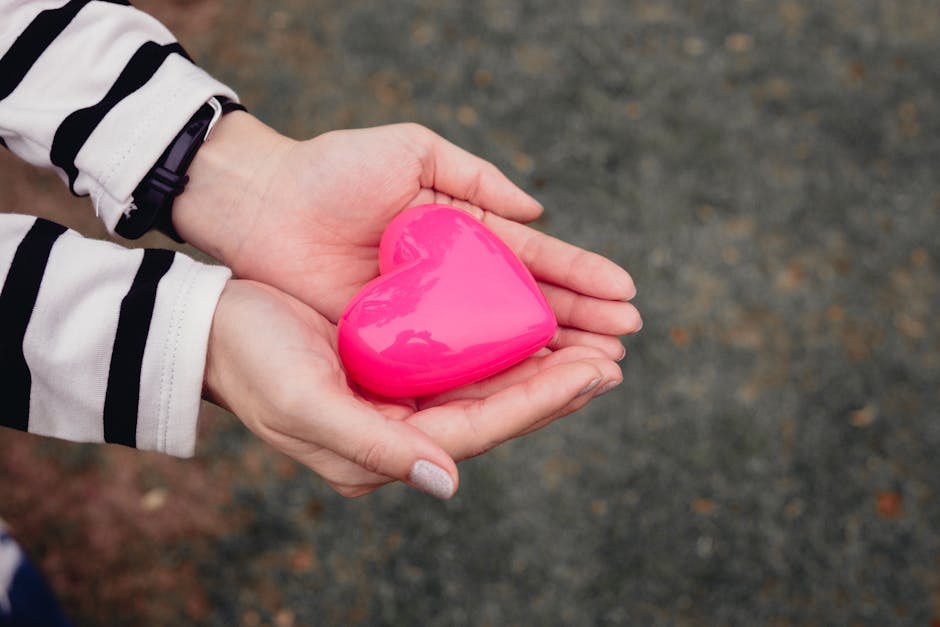 Manifestation gift ideas - Close-up of hands holding a pink heart-shaped toy outdoors, symbolizing love and care.