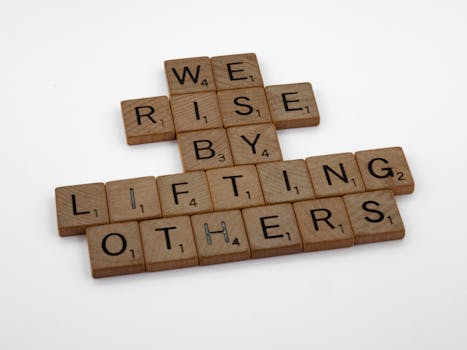 Manifestation gift ideas - Scrabble tiles forming the quote 'We rise by lifting others' on a white background.