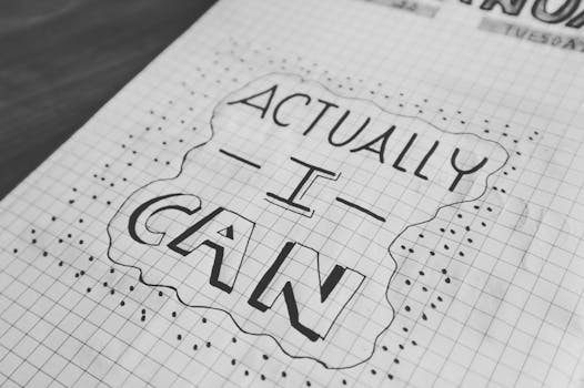 Manifestation Journaling - Motivational text 'Actually I Can' on a grid paper background. Black and white close-up.