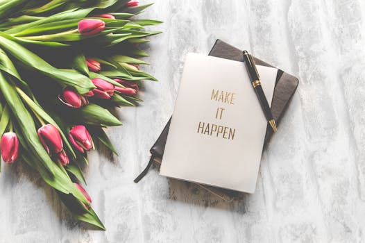 How To Use Manifestation Affirmations To Attract Desires Manifestation Affirmations - A notebook with 'Make It Happen' inscription beside a bouquet of pink tulips, capturing inspiration.