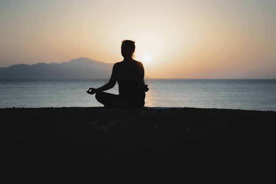 How to Work with Your Energy Field: A Beginner's Guide A woman practices meditation with a tranquil ocean sunset backdrop, embodying peace and relaxation.